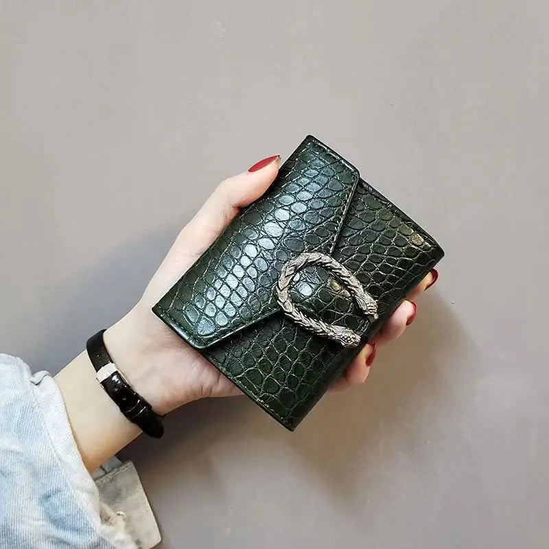 Hand holding a dark green Carauana compact wallet crocodile patterned wallet with a gold buckle