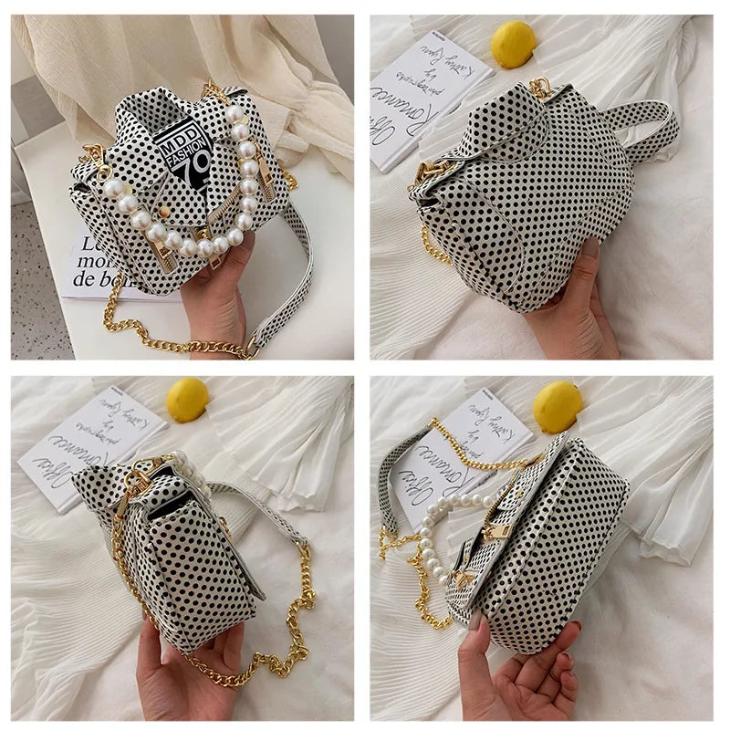 Black and white polka dot handbag with pearl chain held by a hand on a white background.