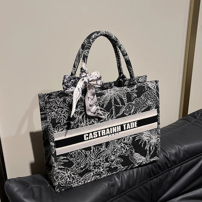 Black floral-patterned tote bag with 'Castrainn Tade' branding on a black surface.