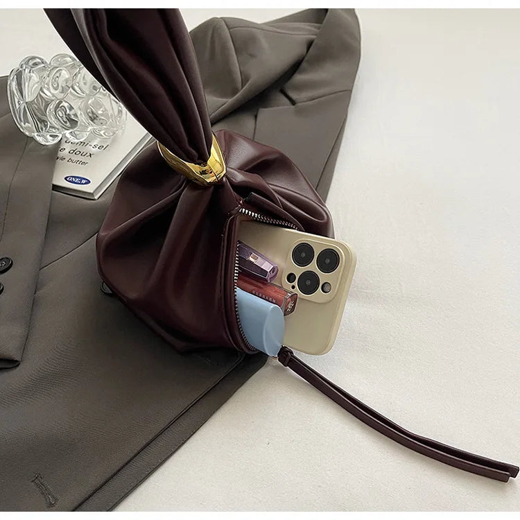 Brown leather pouch with gold clasp on a gray surface