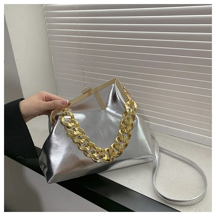 Silver handbag with gold chain handle held by a hand against a neutral background