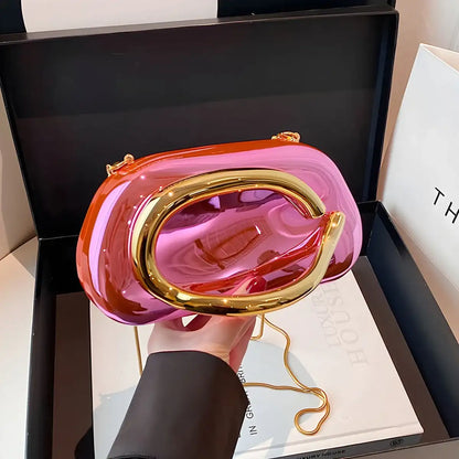 Pink and gold Metallic Carauana Festival Clutch Bag held by a person with a black box and white paper in the background
