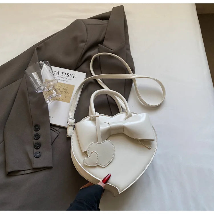 White carauana-lovely-shoulder-bag-heart with bow detail on a surface.